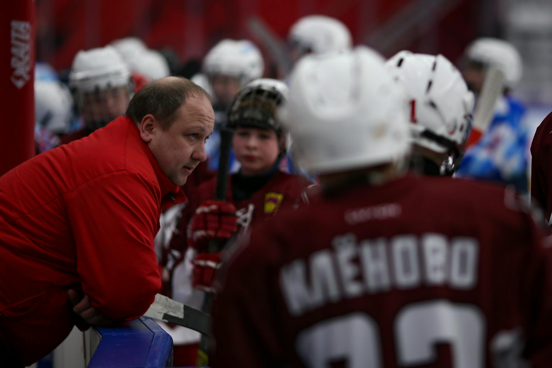 Male trainer talking with children in hockey uniform at ice rink during break of hockey game