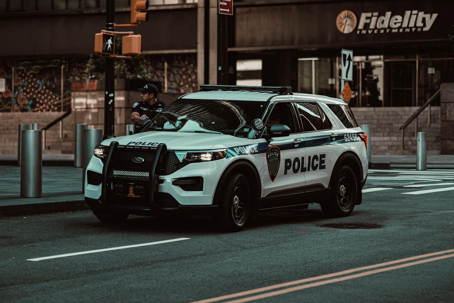 A police car parked on a street in New York City with a policeman nearby, showcasing urban safety.